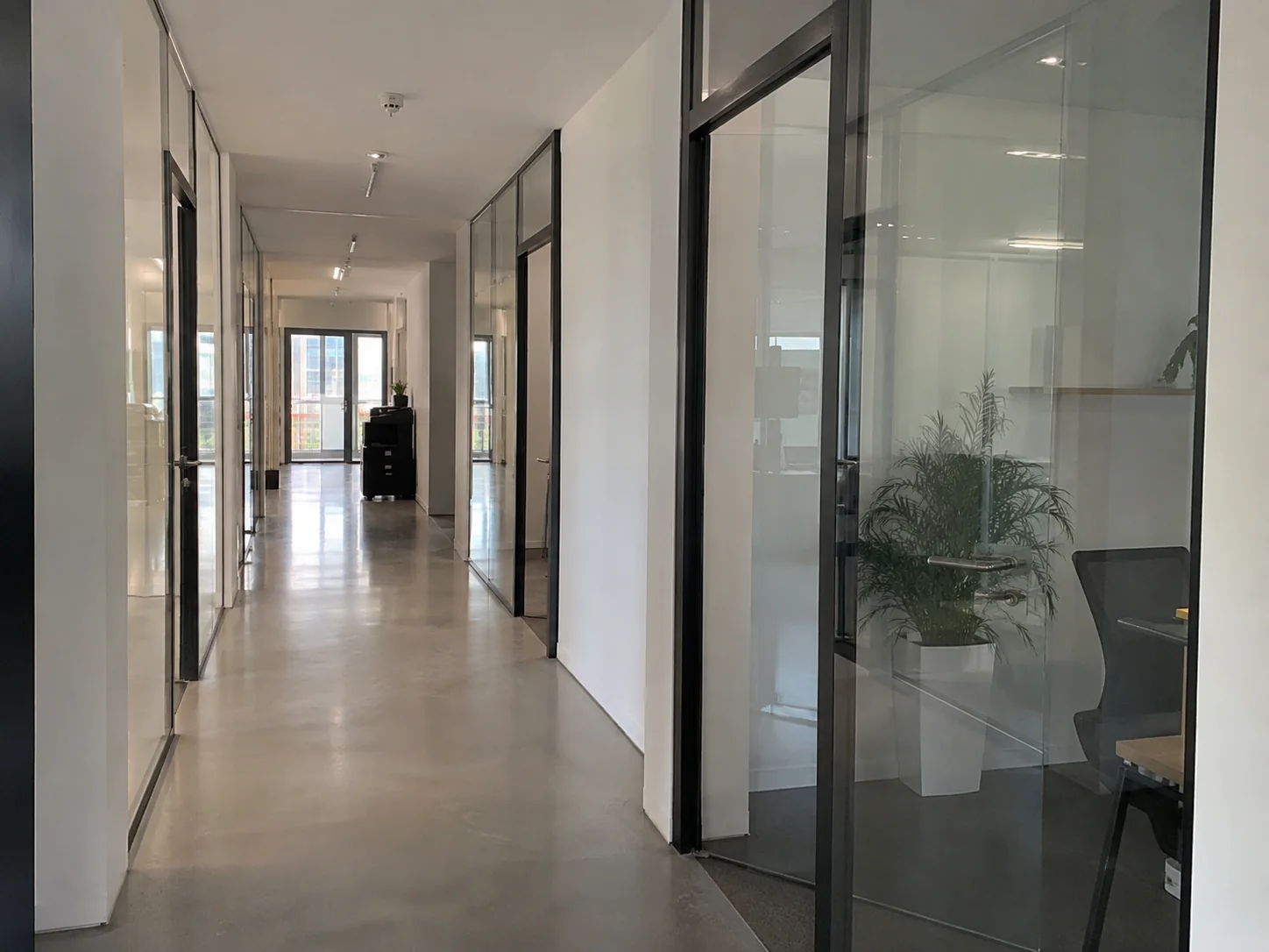 Büroflur mit Glaswänden, seitlichen Büroräumen und hellem Boden