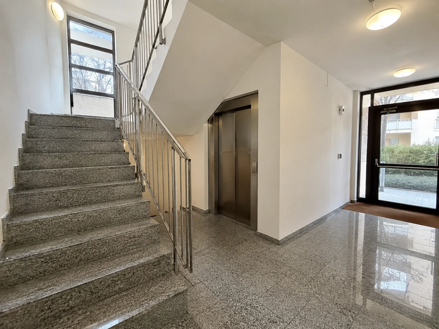 Treppenhaus mit Steinstufen, Aufzug und Glaseingangstür