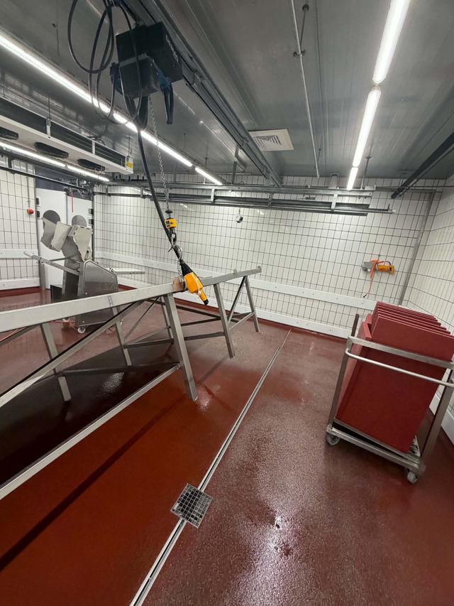 Arbeitsbereich mit Hebevorrichtung, Edelstahlgestellen und rotem Industrieboden